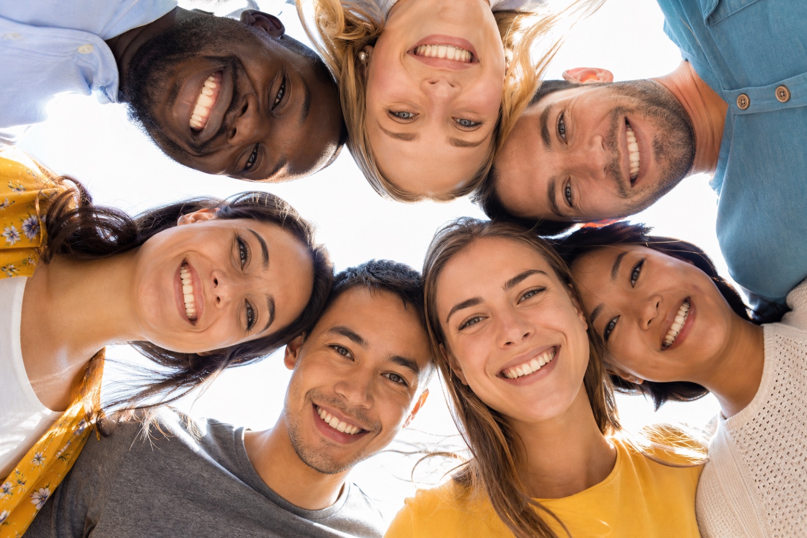 A diverse group of smiling people huddled together looking down at the camera